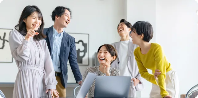 社員がノートパソコンを囲んで笑顔で話している様子